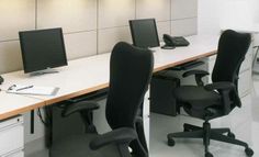 an office cubicle with three computer screens and two chairs in front of the desk