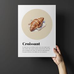 a person holding up a book with an image of a croissant on it