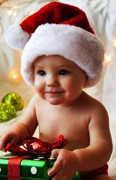 a baby wearing a santa hat sitting next to a christmas present