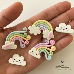 a person is holding several small rainbows and clouds in their palm, with one being held up to the camera