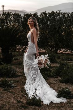 a woman in a wedding dress holding a bouquet and posing for the camera with mountains in the background