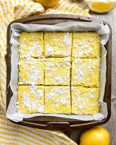 lemon bars with powdered sugar on top in a baking pan next to sliced lemons