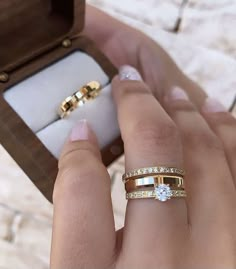 a woman's hand holding two wedding bands and an engagement ring in a box