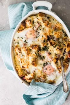 a casserole dish with eggs, cheese and herbs in it on a blue towel