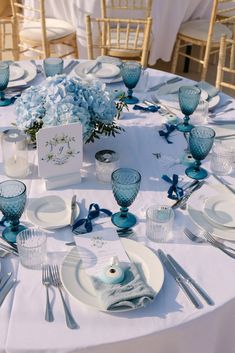 the table is set with plates, silverware and blue flowers