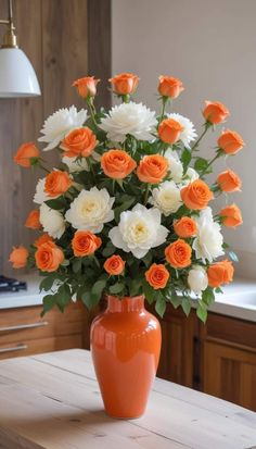 an orange vase filled with white and orange flowers on top of a wooden table in a kitchen