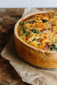 a quiche with cheese and spinach in a pie dish on top of wax paper