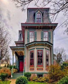 an old victorian style house with red doors and green trim on the front porch, surrounded by greenery