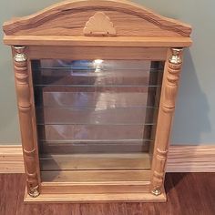 a small wooden shelf with glass doors on the top and bottom, in front of a wall