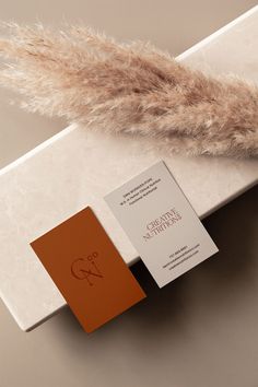 two business cards sitting on top of a white table next to a feather tail and an orange book