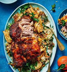 a blue plate topped with meat and pasta next to two bowls of food on top of a blue table cloth