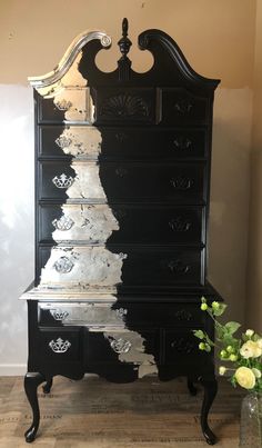 an ornate black dresser with white paint on the top and bottom drawers, next to a flower vase