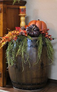 a wooden barrel filled with pumpkins and greenery