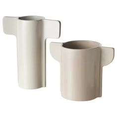 two white vases sitting next to each other on a white surface, one with a curved handle