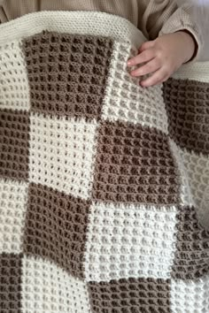 a baby is holding onto a blanket that looks like a checkerboard pattern in brown and white