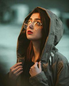 a woman wearing glasses and a hoodie looks off into the distance with her hand on her shoulder