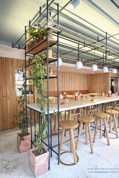 an empty restaurant with tables and stools next to plants on the counter top in front of them