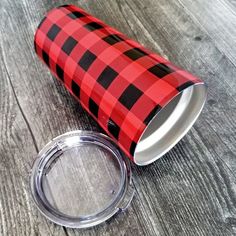 a red and black checkered paper cup next to a metal lid on a wooden table