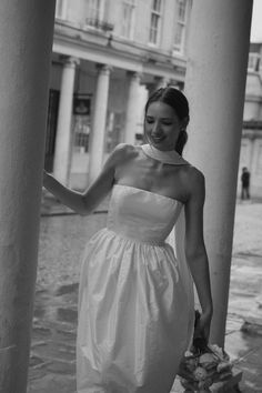 a woman in a white dress is walking down the street with her hand on an object