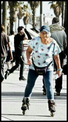 an elderly woman rollerblading down the street with other people in the back ground