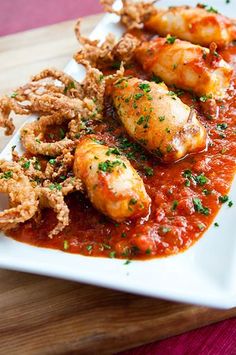 a white plate topped with fried shrimp and marinara sauce on top of a wooden cutting board