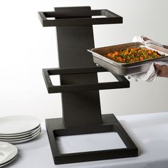 a person holding a tray with food in it on top of a table next to plates