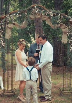 a man and woman standing next to a little boy in front of a wedding arch