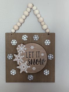 a wooden sign that says let it snow hanging on a wall with white snowflakes