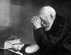 an old man sitting at a table with his hands on his face and looking down