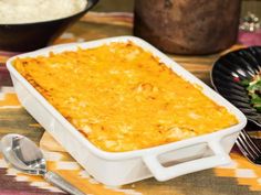 a casserole dish with cheese on top next to a bowl of rice and spoons