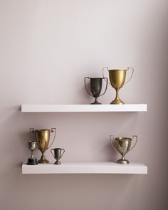 three white shelves with gold and silver cups on them