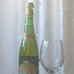 a bottle of wine next to a glass on a window sill with water droplets