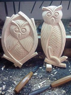 two carved wooden owls sitting on top of a table next to wood shavings