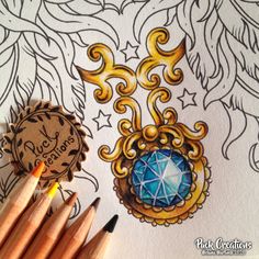 some pencils are laying next to an intricate drawing with a blue diamond in the center