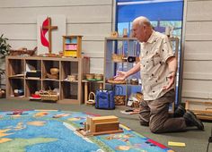 an older man sitting on the floor in front of a room filled with wooden toys