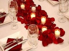 the table is set with red rose petals and candles in the shape of a heart