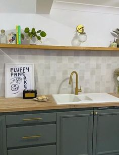 a kitchen with grey cabinets and white tile backsplash, gold faucet