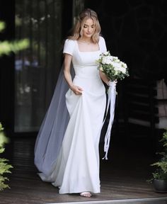 a woman in a white wedding dress is walking down the stairs with her bouquet and veil