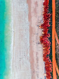 an aerial view of the beach and ocean with orange colored sand, blue water and green grass