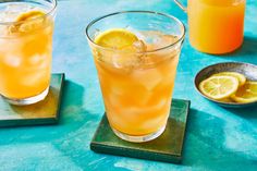 two glasses filled with orange juice and lemon slices on top of coasters next to each other