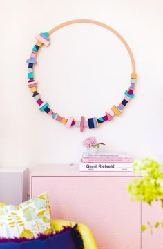 a pink dresser topped with books next to a wall mounted circular art piece on the wall