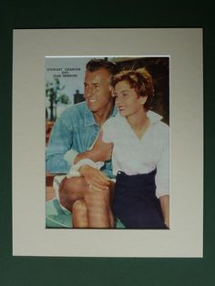 a man and woman sitting next to each other in front of a green wall with a white frame