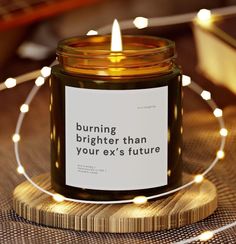 a candle that is sitting on top of a wooden table with some lights around it and the words burning brighter than your ex's future