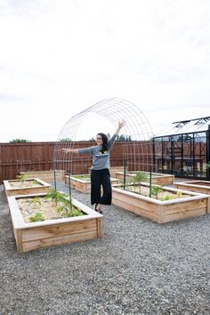 a woman is jumping in the air near some raised beds with plants growing out of them