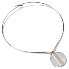 This is a sleek and modern sterling silver neck ring that has a minimalist design. It features a circular silver pendant, which is elegantly simple, with a striking gilded silver strip crossing through its center, adding an authentic touch of character. When worn, it sits gracefully at the base of the neck, complementing the neckline with its clean lines. The neck ring is designed for ease of wear, closing securely with a simple hook mechanism. The combination of silver and gilded silver makes i Modernist Sterling Silver Jewelry With Open Band, Modernist Silver Jewelry With Polished Finish, Modernist Sterling Silver Jewelry Gift, Modernist Silver Necklace For Gift, Neck Ring, Modernist Polished Silver Necklaces, Design Minimalista, Vintage Stil, Vintage Silver