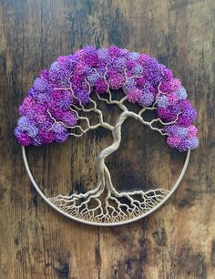 a tree with purple flowers is in a circle on a wooden surface and has roots growing out of it