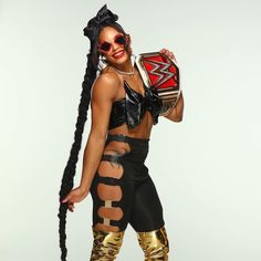 a woman in black and gold outfit holding a wrestling belt with her hands on her hips