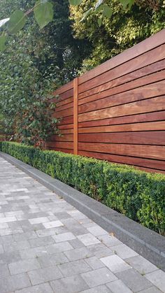 an image of a wooden fence in the middle of a sidewalk with hedges on both sides