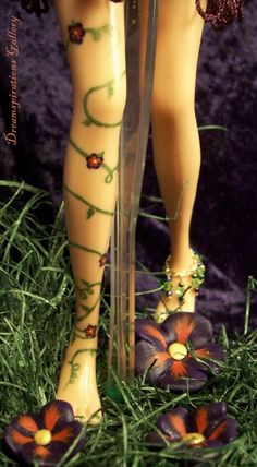 a doll is standing in the grass with her legs crossed and flowers around her ankles