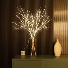 a white vase sitting on top of a green table next to a tree with lights